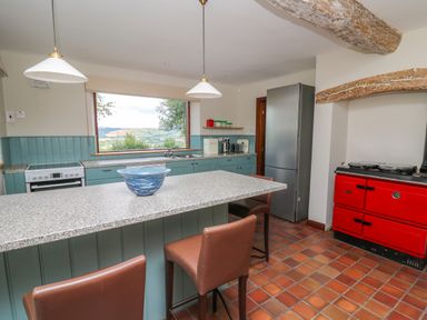 A kitchen with a countertop island and chairs a red stove and a refrigerator at Oak Apple Cottage in Presteigne
