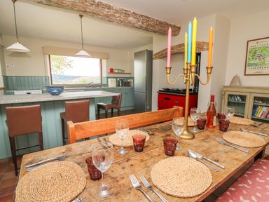 A kitchen and dining area with a wooden table set for six and a red stove at Oak Apple Cottage in Presteigne