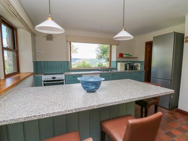 A kitchen with a large island and brown chairs a stove a refrigerator and a window with a countryside view at Oak Apple Cottage in Presteigne