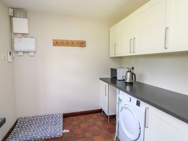 A utility room with a washing machine microwave kettle and a dog bed at Oak Apple Cottage in Presteigne