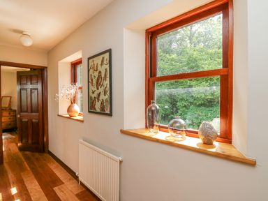 A hallway with wooden floors and two windows with vases on the sills at Oak Apple Cottage in Presteigne