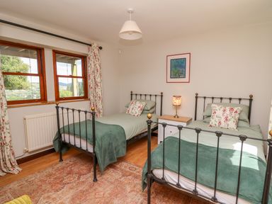 A bedroom with two single beds with green covers and floral pillows and a nightstand with a lamp between them at Oak Apple Cottage in Presteigne
