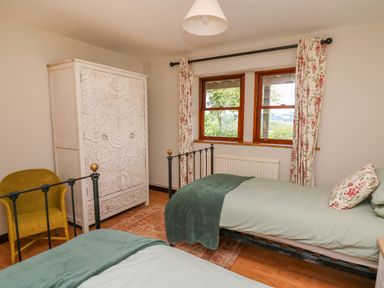 A bedroom with two single beds green bedding carved white wardrobe and yellow chair at Oak Apple Cottage in Presteigne