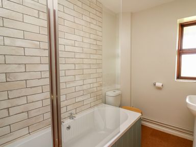 A bathroom with a bathtub shower toilet and window at Oak Apple Cottage in Presteigne
