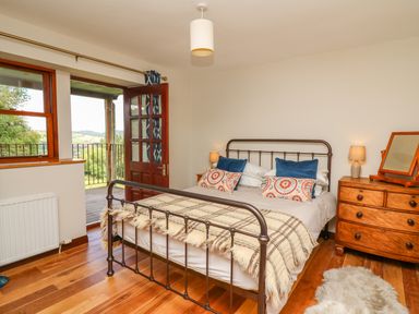 A bedroom with a metal bed frame two bedside tables with lamps a chest of drawers and an open door leading to a balcony at Oak Apple Cottage in Presteigne