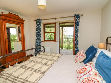 A bedroom with a bed pillows a wooden wardrobe and a door leading to a balcony at Oak Apple Cottage in Presteigne