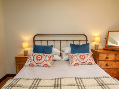 A bedroom with a metal bed frame two bedside tables with lamps and a dresser with a mirror at Oak Apple Cottage in Presteigne