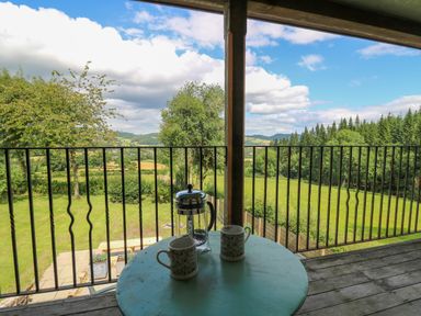A patio table with two mugs and a French press on a balcony overlooking a garden and countryside at Oak Apple Cottage in Presteigne