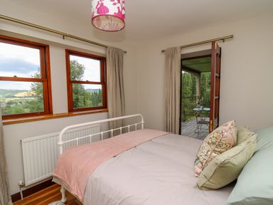 A bedroom with a bed and pillows next to two windows and a door leading to a balcony at Oak Apple Cottage in Presteigne
