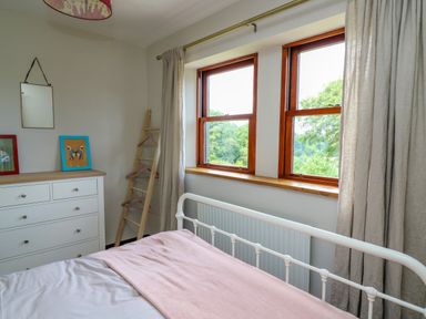 A bedroom with a bed near two windows a white dresser with framed pictures and a clothes ladder Oak Apple Cottage Presteigne
