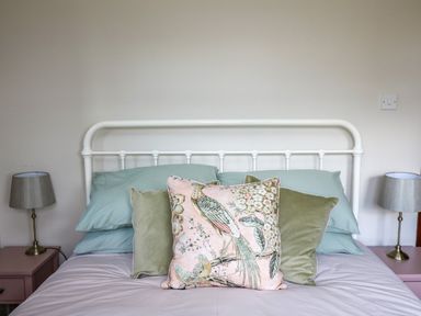 A bed with pastel green pillows and a decorative pillow with bird design and two bedside tables with lamps at Oak Apple Cottage in Presteigne