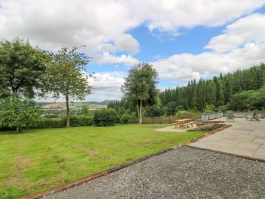 An outdoor area with lawn trees picnic bench and patio with chairs in a rural setting at Oak Apple Cottage in Presteigne