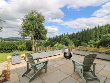 A patio with two chairs and planters overlooking trees and hills at Oak Apple Cottage in Presteigne