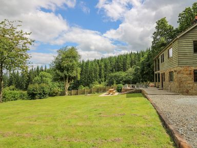 A grassy yard with trees and picnic table next to a gravel driveway and stone house at Oak Apple Cottage in Presteigne