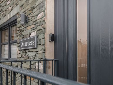 Stone wall with a window and a sign reading Quarters next to a dark colored door at Quarters in Ambleside