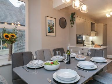 A dining table set with plates glasses and cutlery near a kitchen with cabinets and a window with sunflowers at Quarters in Ambleside