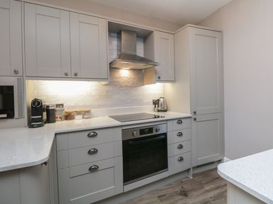 A kitchen with grey cabinets a built in oven an electric stovetop and appliances on the countertop at Quarters in Ambleside