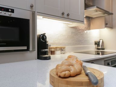 A kitchen counter with bread on a wooden cutting board and a knife with an electric kettle and coffee machine in the background at Quarters Ambleside