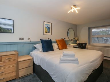 A bedroom with a bed with blue and orange pillows wooden drawers a desk with a round mirror and a window at Quarters in Ambleside