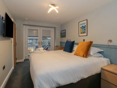 A bedroom with a large bed with two pillows a TV on the wall and glass doors at Quarters Ambleside