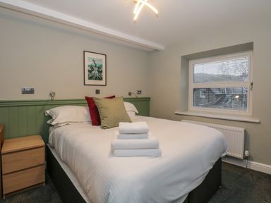 A bedroom with a double bed two pillows folded towels a wooden bedside table and a window with blinds at Quarters in Ambleside