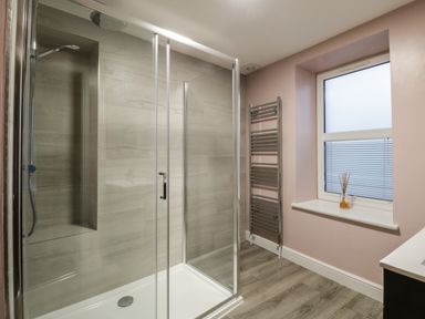 A bathroom with a glass shower enclosure a heated towel rail and a window at Quarters in Ambleside