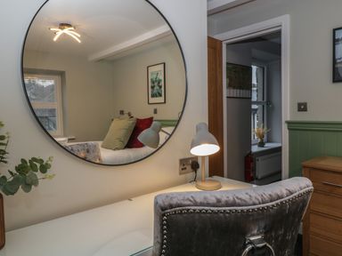 A bedroom reflected in a round mirror showing a bed with pillows a lamp on a desk and a chair at Quarters in Ambleside