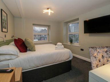 A bedroom with a bed with pillows and folded towels a wall mounted television and two windows with blinds at Quarters in Ambleside