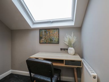 A small desk with a chair below a skylight window and a framed map on the wall with a vase of pampas grass on the desk at Quarters Ambleside