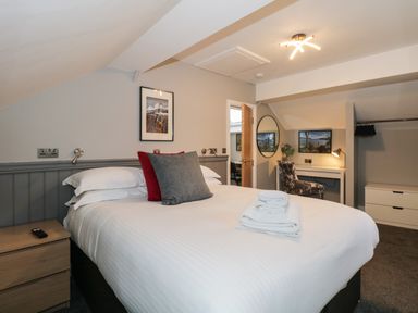 A bedroom with a bed pillows and towels a desk with a lamp and chair and a wall mirror at Quarters in Ambleside