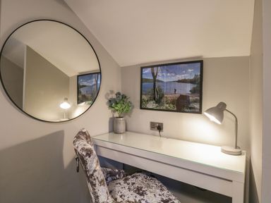A desk with a lamp and a vase of flowers under a framed picture and a round mirror on the wall at Quarters in Ambleside