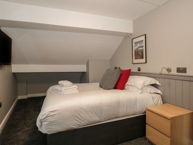 A bedroom with a double bed with pillows and folded towels a wooden bedside cabinet and a wall-mounted television at Quarters in Ambleside
