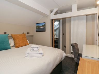 A bedroom with a bed with pillows and folded towels a chair and a desk with a mirror at Quarters in Ambleside