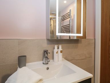 A bathroom sink with a chrome faucet white towel gray cup and two soap dispensers under a mirror at Quarters in Ambleside