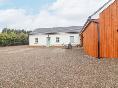 An exterior view of a white building with green door and windows next to a wooden structure with outdoor chairs and table near some trees at Curhoor Near Loughrea County Galway