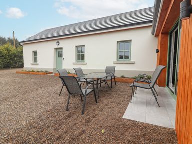 An outdoor patio area with a glass table and six chairs outside a white building with green windows at Curhoor Near Loughrea County Galway