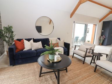 A living room with a navy sofa with cushions a round mirror above a black coffee table with plants and candles two beige armchairs a sliding glass door and wooden ceiling beams at Curhoor Near Loughrea County Galway