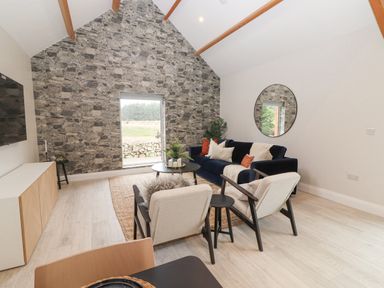 A living room with stone accent wall window blue sofa chairs round mirror and TV at Curhoor Near Loughrea County Galway