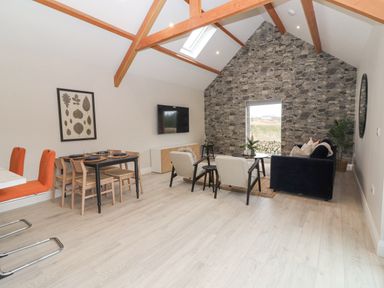 A living room with a stone wall and window with blue sofa beige armchairs dining table with chairs and orange stools at Curhoor Near Loughrea County Galway
