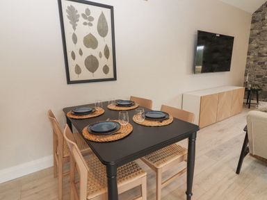 A dining area with a black table set for four with blue plates and glasses near a modern cabinet and wall mounted TV at Curhoor Near Loughrea County Galway