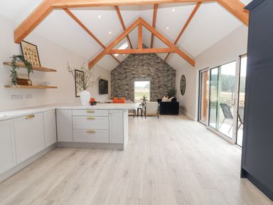 An open kitchen and living area with wooden beams a stone accent wall and sliding glass doors at Curhoor Near Loughrea County Galway