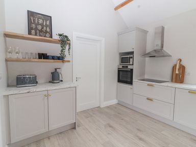 A kitchen with white cabinets wooden shelves holding glasses and mugs a toaster kettle oven microwave and stove at Curhoor Near Loughrea County Galway