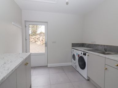 A laundry room with a washing machine dryer sink and cabinets near a door with a view outside at Curhoor Near Loughrea County Galway