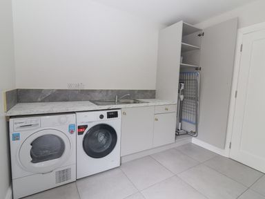 A laundry room with washing machine dryer sink and an open cabinet storing cleaning tools at Curhoor Near Loughrea County Galway