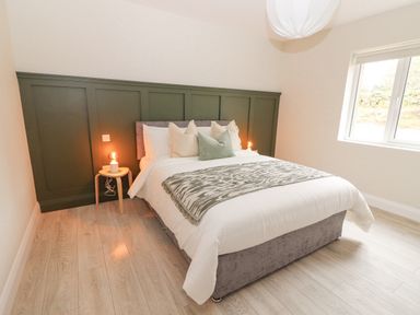 A bedroom with a bed with pillows and a blanket with a green paneled wall and a window at Curhoor Near Loughrea County Galway