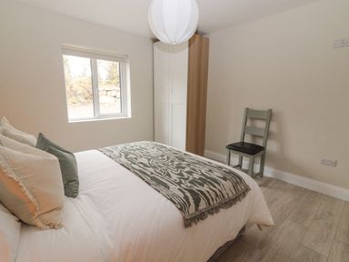 A bedroom with a bed pillows and a patterned throw a window a wardrobe and a chair at Curhoor Near Loughrea County Galway