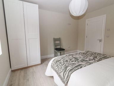 A bedroom with a bed a patterned throw a white wardrobe a gray chair and a closed door at Curhoor Near Loughrea County Galway