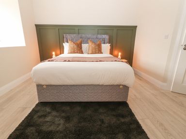 A bedroom with a bed brown pillows two lamps on a green panel wall and a dark rug on wooden floor at Curhoor Near Loughrea County Galway