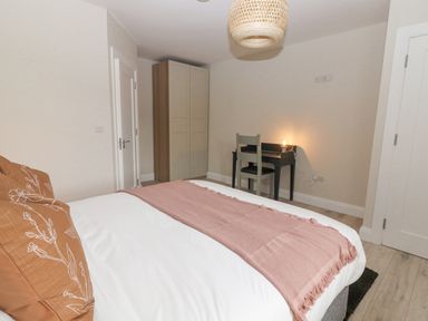 A bedroom with a bed linens pillows pink throw blanket wardrobe desk and chair with lamp at Curhoor Near Loughrea County Galway