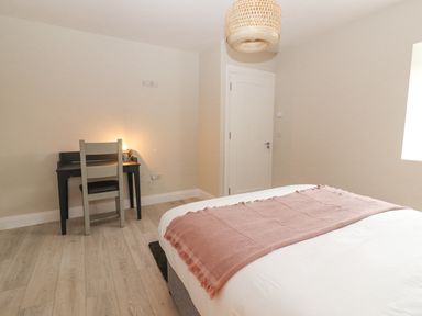 A bedroom with a bed with a pink blanket and a small desk with a chair and lamp at Curhoor Near Loughrea County Galway